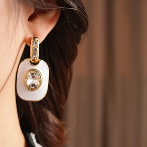 Gros plan d'une boucle d'oreille vintage dorée avec émail blanc et strass brillant