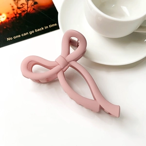 Detailed close-up of a pink matte bow hair claw clip placed on a white desk