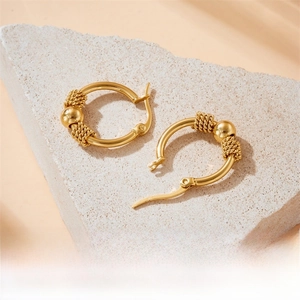 Close-up of gold-plated stainless steel hoop earrings with textured beads on a stone