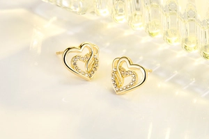 Macro view of gold heart stud earrings featuring interlocking hollow hearts with pavé zircon