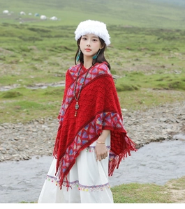 Close-up of red ethnic poncho with geometric patterns and fringe detail in nature