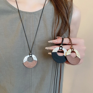 Detail of geometric wood and metal pendant necklace worn over linen clothing