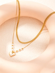 Dettaglio di una collana dorata a doppio strato con ciondolo a cuore e perla finta