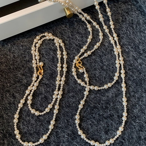 Detail of elegant pearl necklace strands featuring a gold S-hook clasp on plush fabric