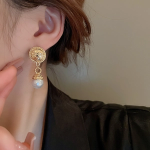 Detail of vintage French style gold earrings with circular texture and pearl drop pendant