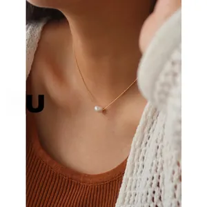 Close-up of a single white pearl pendant on a thin gold chain worn by a female model