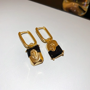 Close-up of vintage gold earrings with lion head relief and black geometric inlay