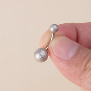 Close-up of a frosted silver stainless steel belly button ring held by hand