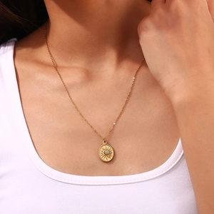 Detail of 18K gold-plated oval sun pendant necklace with green stone on a model
