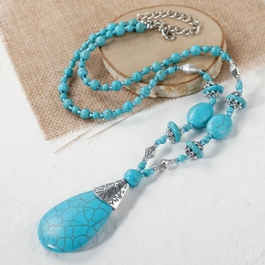 Macro shot of bohemian turquoise beaded necklace with drop pendant on rustic wood base
