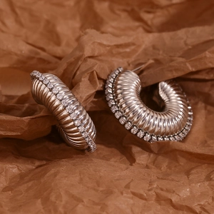 Macro view of silver hollow twisted earrings with zircon edges on brown paper background