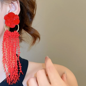 Close-up of red floral earrings with long beaded tassels worn by a model in warm light