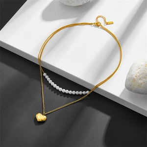 Detail of double-layer necklace with gold heart pendant and white pearls on steel chain