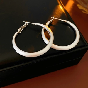 Close-up of matte silver geometric hoop earrings on black leather texture