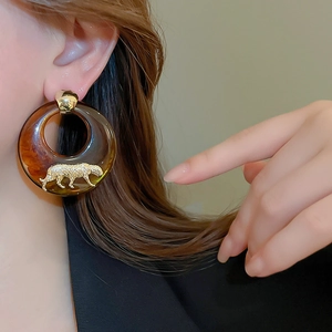 Detailed close-up of brown resin earrings featuring a gold panther sculpture and golden stud