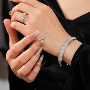 Macro detail of silver flower ring and textured clover engraved bangle on black fabric
