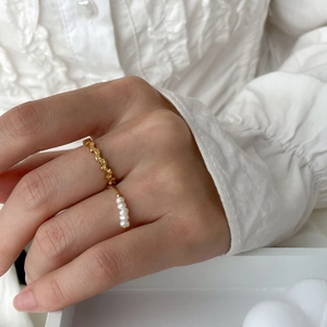 Detail of a minimalist gold wavy pearl ring worn on hand with a white pleated shirt