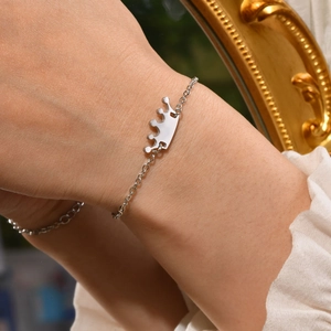 Detailed close-up of a silver crown charm bracelet worn on a wrist with a vintage mirror background