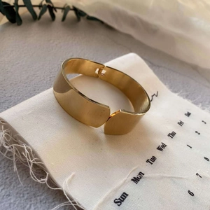 Polished gold-plated wide cuff bangle on white linen fabric with minimalist aesthetic