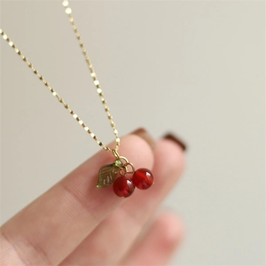 Detailed view of cherry pendant necklace with red crystal beads and green leaf on gold chain