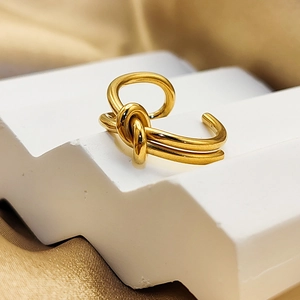 Macro detail of 18K gold plated stainless steel knot ring on a white geometric stand