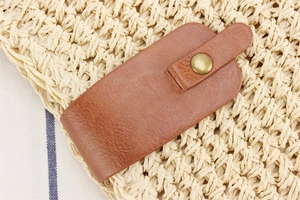 Detail shot of brown lychee grain leather buckle with bronze snap on straw bag