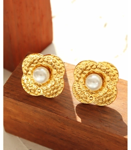 Detail of 18K gold-plated clover earrings with white pearl on a natural wooden block