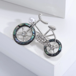 Detail of silver bicycle brooch featuring sparkling rhinestones and a white pearl accent