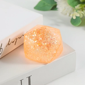 Macro view of an orange polyhedral stress relief toy with gold glitter on a white book