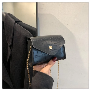 Close-up of black crocodile pattern leather texture with gold chain strap and button