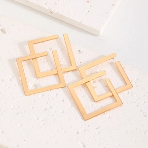 Detailed close-up of golden geometric double square earrings on a textured stone surface