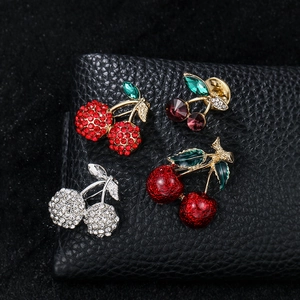 Detail showing various cherry brooches with rhinestones and enamel on black leather surface