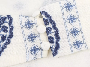 Detail of white cotton dress featuring blue geometric embroidery and fabric buttons