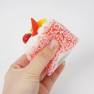 Pink heart mousse cake squishy toy with cream and fruit decor being squeezed by hand