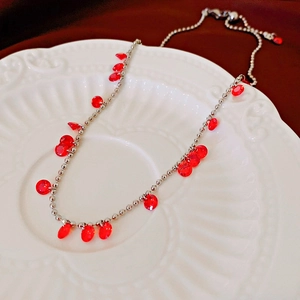 Collier vintage chaîne à billes argentée avec pendentif en cristal rouge sur assiette blanche