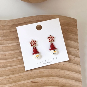 Close-up of Christmas earrings with red stars and small snowmen on a wooden display