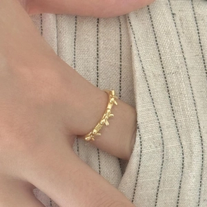 Close-up of model wearing gold bow-shaped ring on light textured fabric background