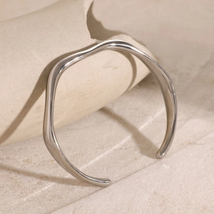 Macro shot of silver stainless steel wavy open bangle with polished reflective surface