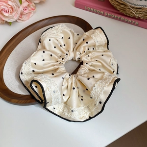 Gros plan d'un chouchou en satin crème à pois avec bordure en dentelle délicate