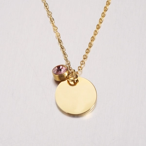 Close-up of golden stainless steel circle pendant with small pink birthstone charm on chain
