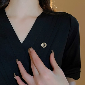 Close-up of elegant gold brooch with pearls and interlocked design on black garment