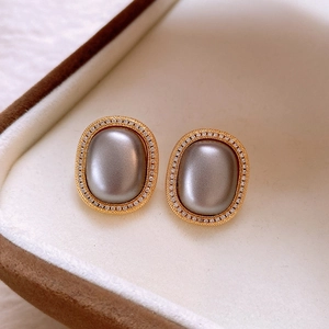 Macro detail of oval gray gemstone earrings with gold borders and clear crystal accents