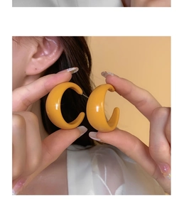 Close-up of mustard yellow acrylic C-shape chunky earrings held by model for display