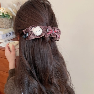 Détail d'une pince à cheveux à carreaux marron avec ours en peluche et nœud rouge