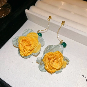 Detail of yellow fabric rose earrings with light blue leaves and gold hooks on white display