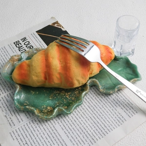 Detail of green wavy resin tray with gold foil flakes and croissant decor on magazine