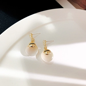 Detail of elegant gold earrings with white cat-eye stones on a white ceramic plate