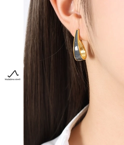 Close-up of C-shaped golden stainless steel earrings with dark enamel and hammered texture