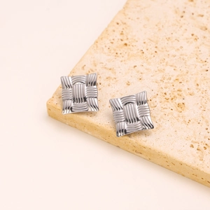 Detail view of silver square earrings with woven texture on a beige stone slab