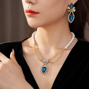 Close-up of pearl necklace and bow earrings with blue teardrop stones and rhinestones